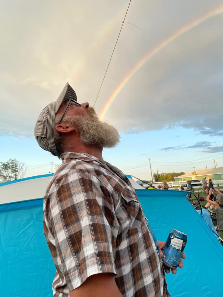 A man posing for a photo with a rainbow in the background so it appears that it is coming from his mouth