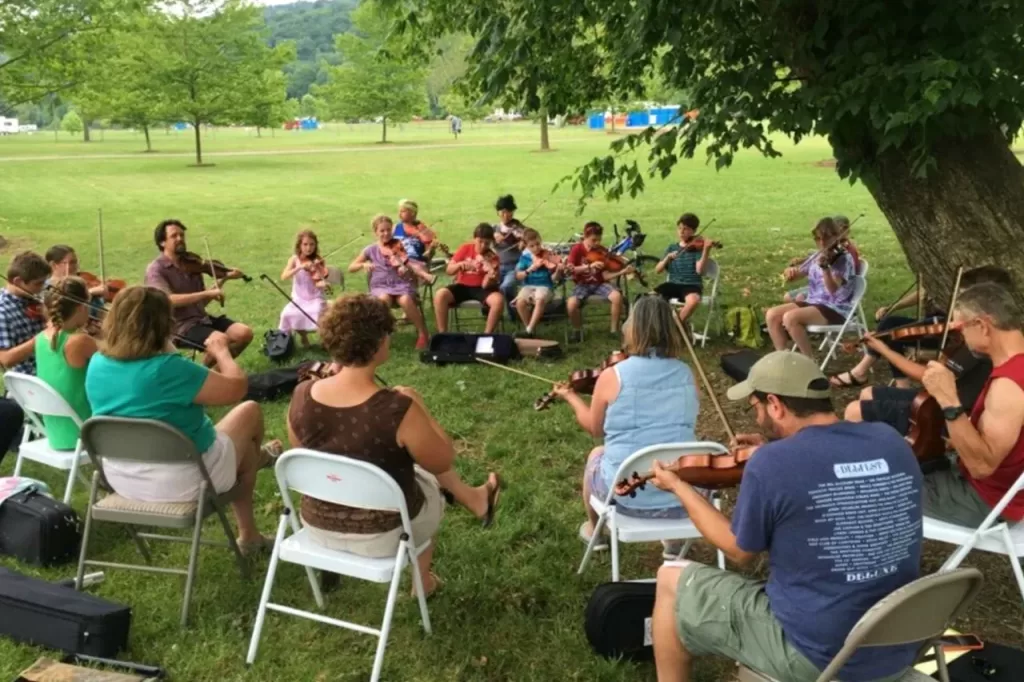 Fiddle workshop participants at River and Roots seated in a circle playing together.