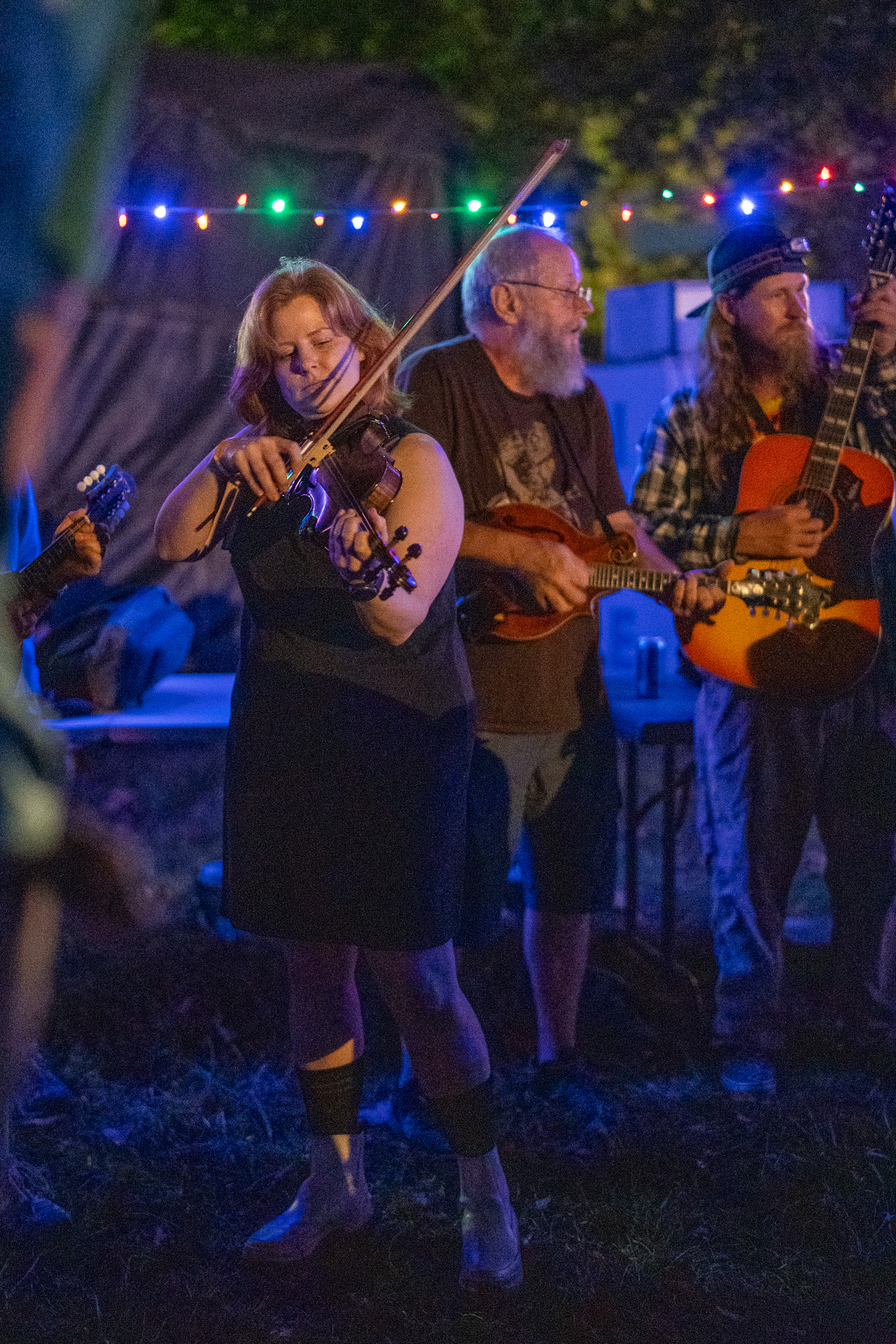 Neurology Fiddler – photo by John Cromartie a woman playing fiddle with a mandolin player and guitarist in the background at the Neurology Jam