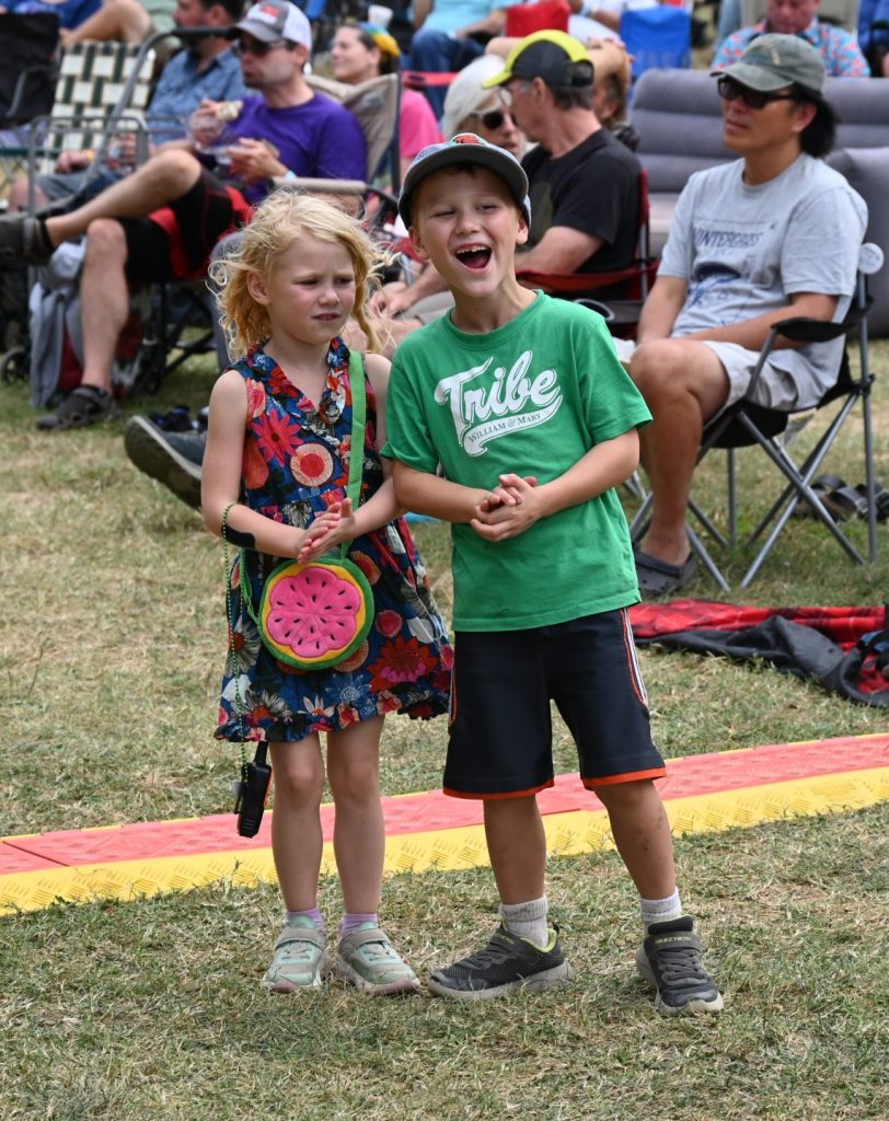 Children, two little boys and a girl, dance and play in front of the stage at the 2025 Watermelon Pickers' fest