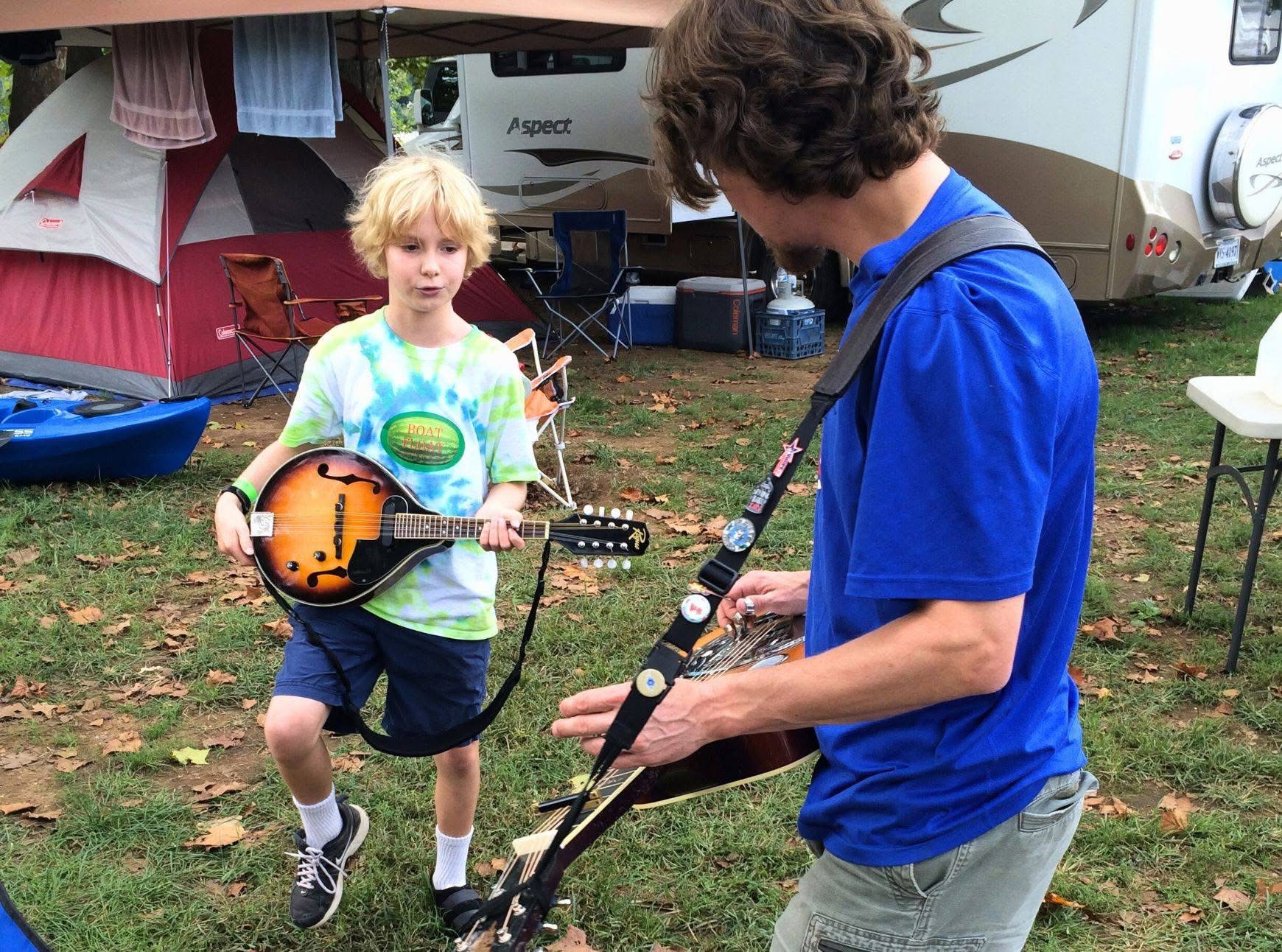 A kid and his friend playing music at a campsite